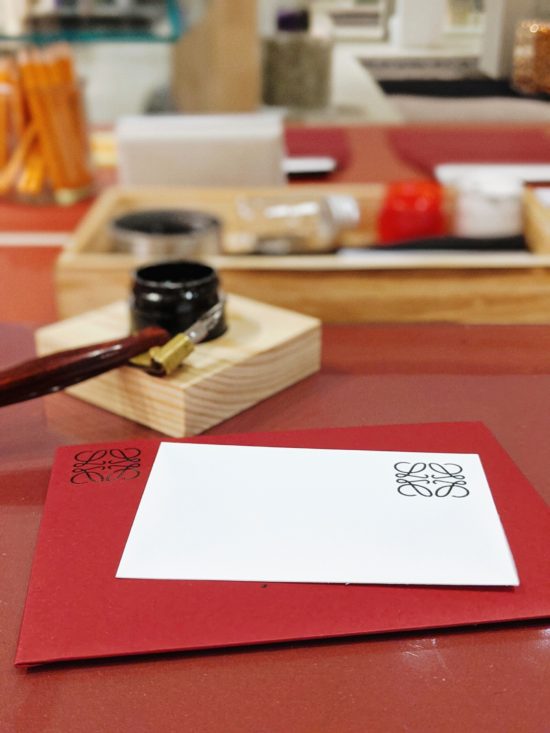 Blank white card on top of red envelope with pointed pen set up in the background.