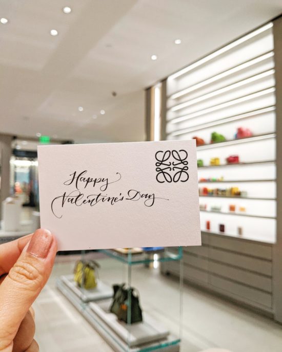 Hand holding a card with "Happy Valentine's Day" written in beautiful calligraphy.