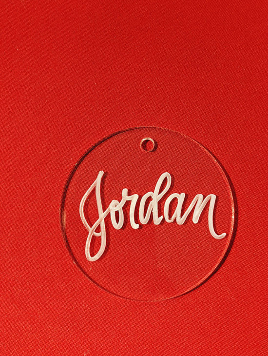 Clear acrylic holiday ornament with the name "Jordan" written in red ink.